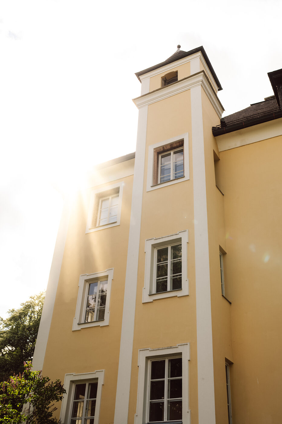 Die gelbe Fassade von Schloss Wiespach mit Turm im Gegenlicht.